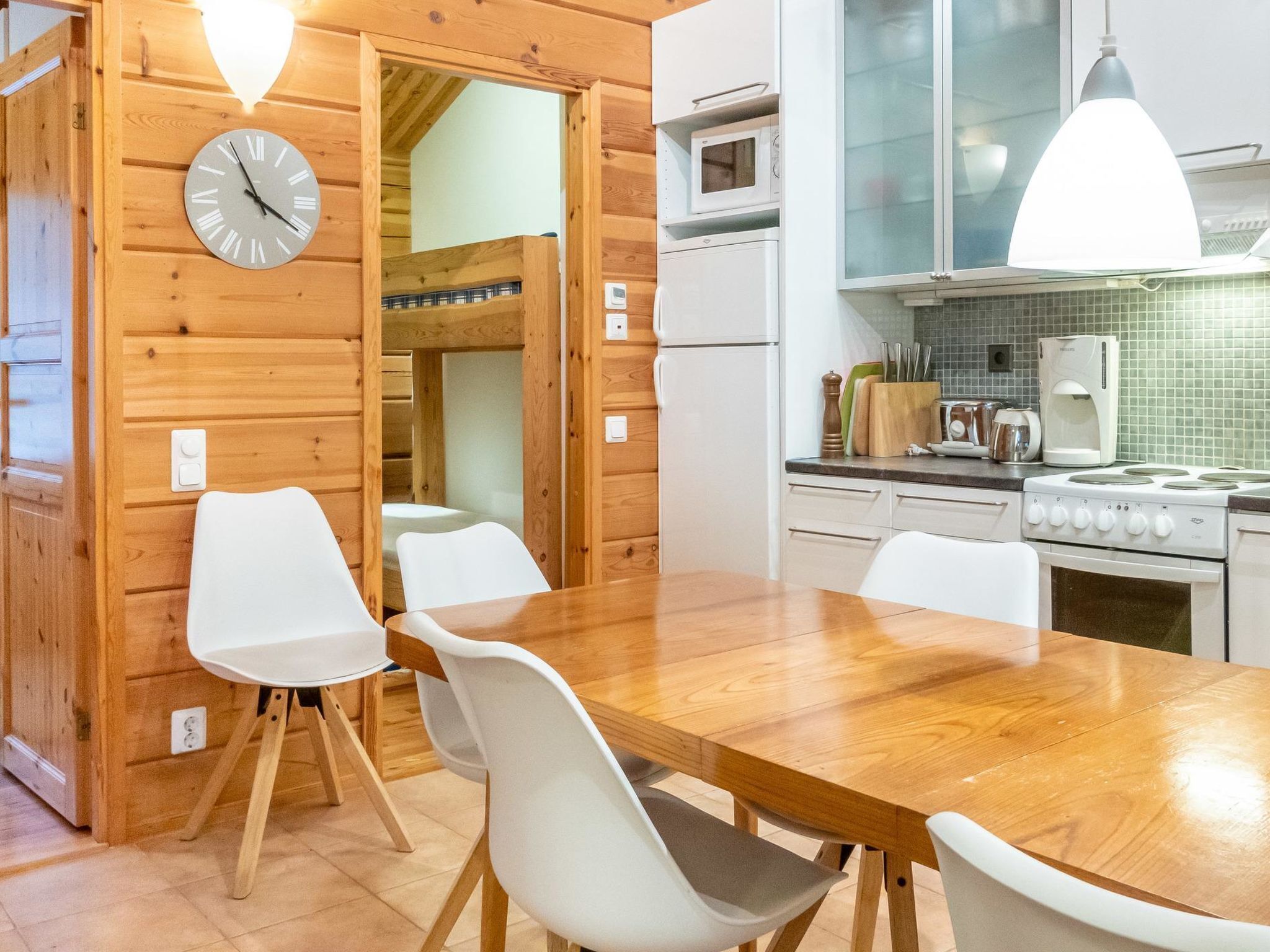 A wooden interior with a dining table, chairs, a clock, a microwave, and a stove.