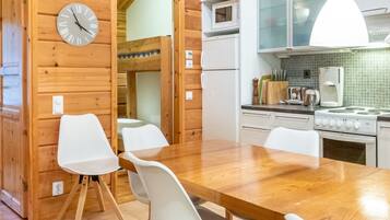 A wooden interior with a dining table, chairs, a clock, a microwave, and a stove.
