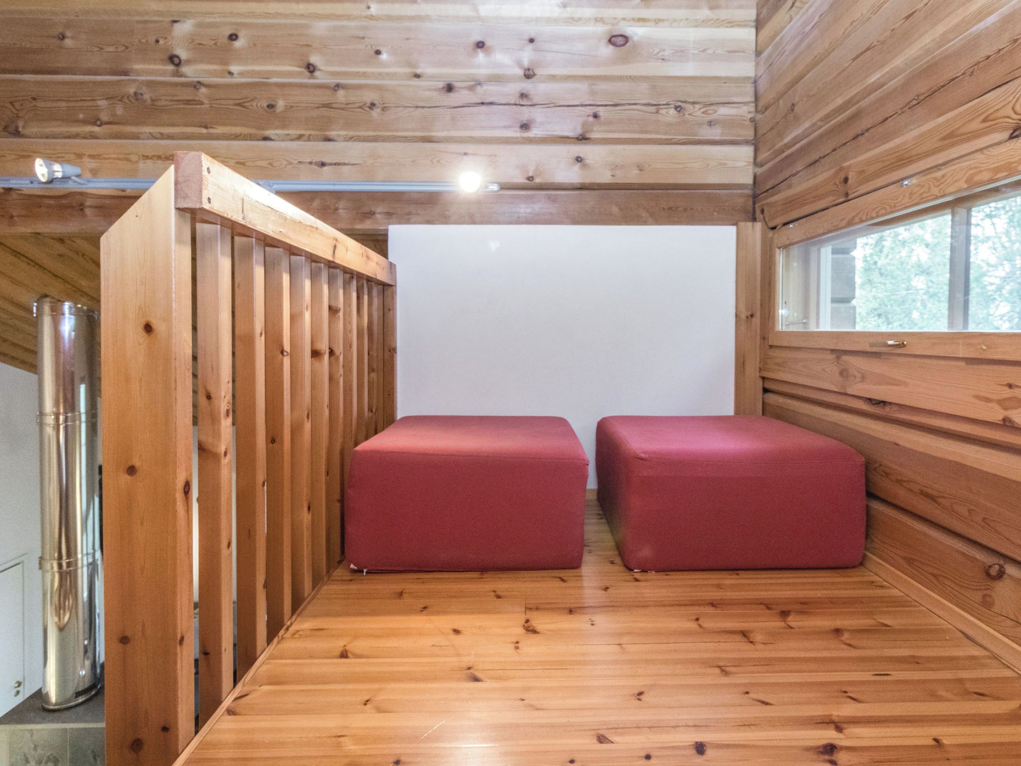 A room with wooden walls and a wooden floor, featuring two red cushioned seating areas and a large window.
