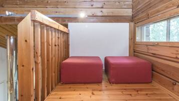 A room with wooden walls and a wooden floor, featuring two red cushioned seating areas and a large window.