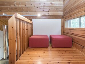 A room with wooden walls and a wooden floor, featuring two red cushioned seating areas and a large window.