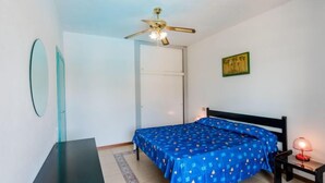 A bedroom with a bed, a desk, a ceiling fan, a door, and a small table with a lamp. - Bilo Standard by Interhome (Marina di Bibbona)