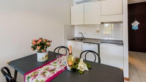 A compact kitchen with white cabinets, a built-in oven, and a small sink. A dining table with chairs is set with a floral table runner, a bottle of wine, and glasses. - Bilo Standard by Interhome (Marina di Bibbona)