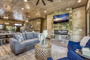 A cozy living room with a stone fireplace, a large TV mounted on the wall, and a comfortable seating area with a sofa and armchairs.