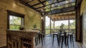 Interior em madeira com área de bar, mesas ao ar livre e grandes janelas.
