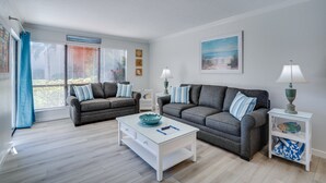 A living room with two grey sofas, a white coffee table, and a side table with a lamp. - Runaway Bay 112 by SeaBreeze Vacation (Bradenton Beach)