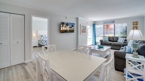 A modern living room with a white dining table, grey sofa, and blue and white decor. - Runaway Bay 112 by SeaBreeze Vacation (Bradenton Beach)