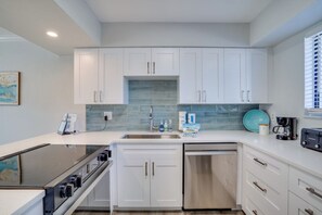 Une cuisine moderne avec des meubles blancs, un lave-vaisselle en acier inoxydable et une cuisinière encastrée.
