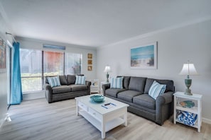 Un salon avec deux canapés gris, une table basse blanche et une table d’appoint avec des lampes.