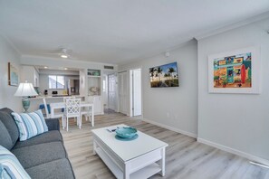 Een moderne woonkamer met een witte salontafel, een grijze bank en een eethoek met witte stoelen.