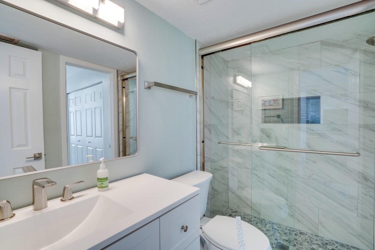 A bathroom with a white sink, a mirror, a glass shower enclosure, and a toilet.