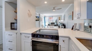 A modern kitchen with a built-in oven and microwave, white cabinetry, and a dining area with a table and chairs. - Runaway Bay 112 by SeaBreeze Vacation (Bradenton Beach)