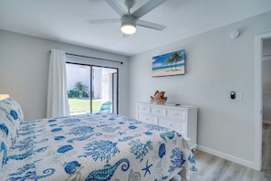 Een slaapkamer met een bed, een plafondventilator, een raam met gordijnen, een schilderij, een dressoir en een deur naar een balkon.
