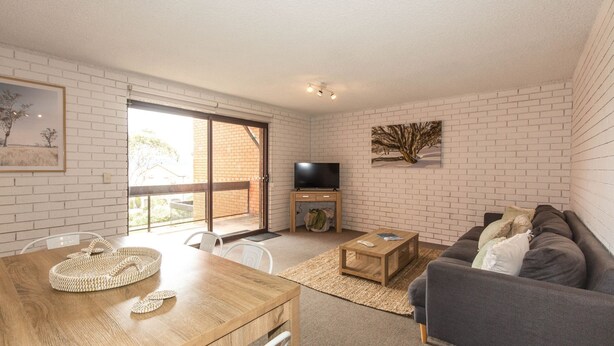 A modern living room with a wooden dining table, a grey sofa, and a TV on a wooden stand. - Sunrise - 15/121 Gippsland Street (Jindabyne)