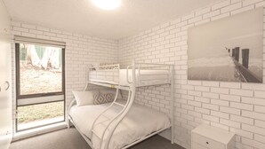 A room with a bunk bed, a window with a view of trees, a white brick wall, and a small white nightstand. - Sunrise - 15/121 Gippsland Street (Jindabyne)