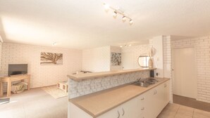 A modern kitchen with white brick walls, a marble countertop, and a built-in sink. - Sunrise - 15/121 Gippsland Street (Jindabyne)