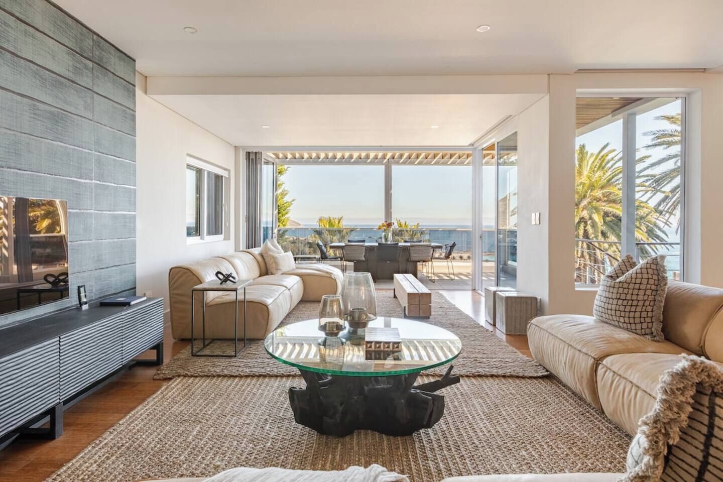A modern living room with a glass coffee table, leather sofas, and a view of the ocean.