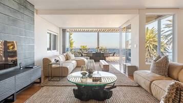 A modern living room with a glass coffee table, leather sofas, and a view of the ocean.