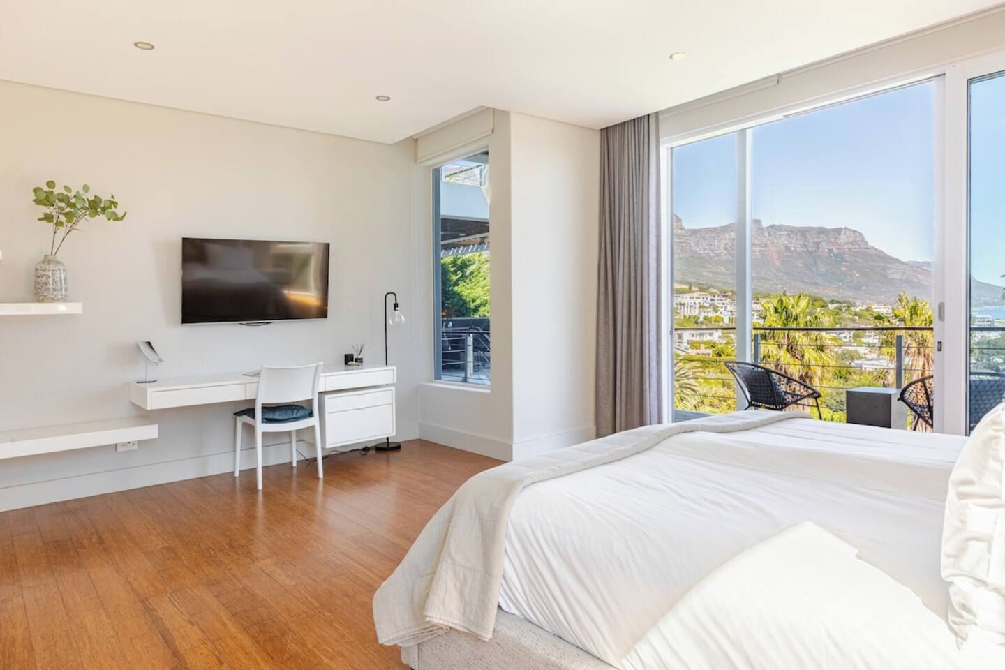 Une chambre moderne avec un grand lit, un bureau, une chaise, une télévision et un balcon offrant une vue sur le paysage.