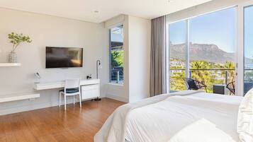 Une chambre moderne avec un grand lit, un bureau, une chaise, une télévision et un balcon offrant une vue sur le paysage.