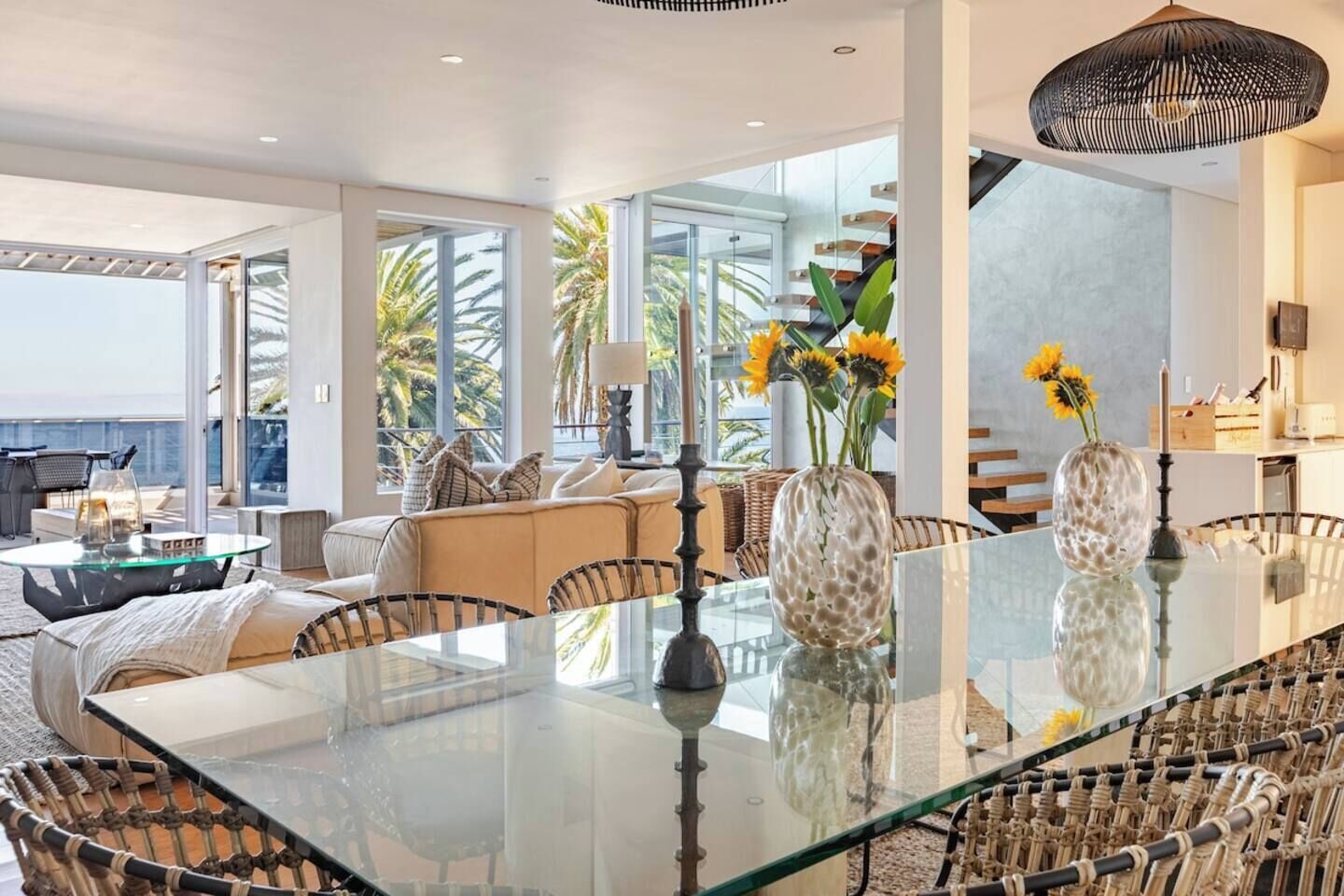 A modern living room with a glass dining table, wicker chairs, and a sofa.