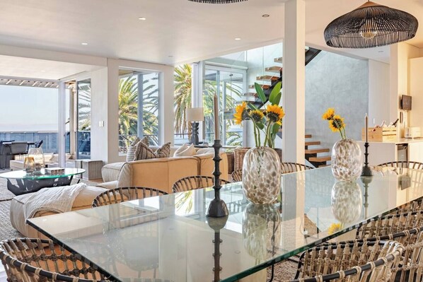 A modern living room with a glass dining table, wicker chairs, and a sofa.