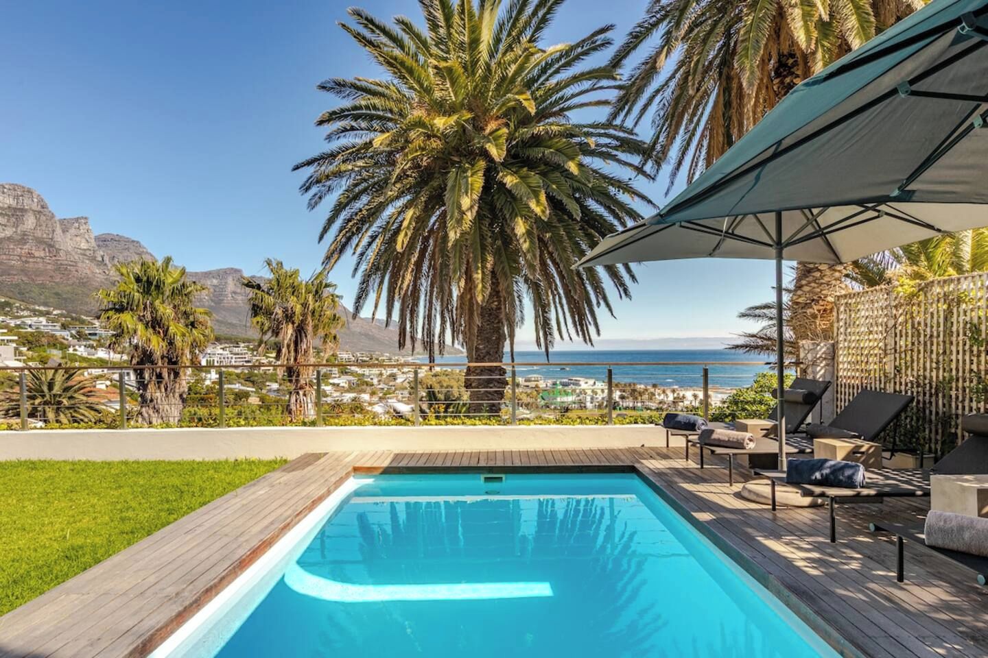 Une piscine avec une terrasse en bois, des chaises longues et une vue sur l’océan et les montagnes.