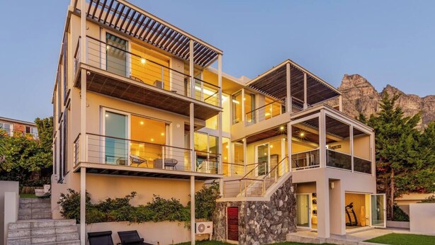 Una casa moderna de varios pisos con piscina, mobiliario exterior y vista a las montañas.