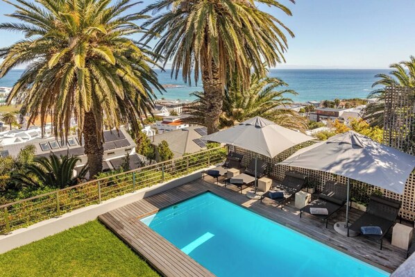 A pool area with a view of the ocean, surrounded by palm trees and a wooden deck.