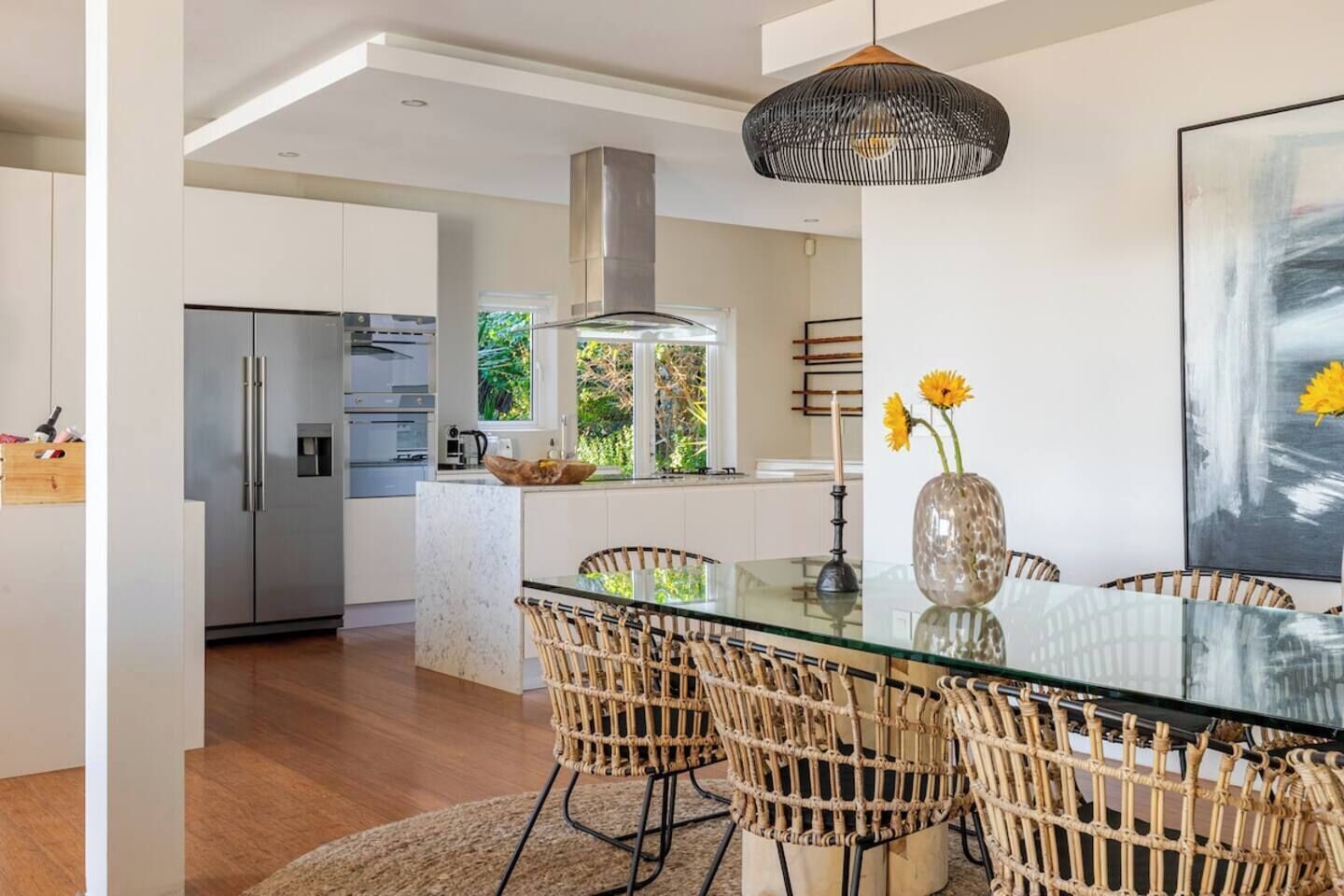 Una cocina moderna con una mesa de vidrio, sillas de mimbre y una lámpara colgante.