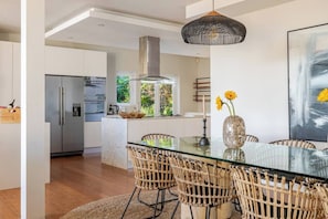A modern kitchen with a glass dining table, wicker chairs, and a pendant light.