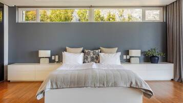 A modern bedroom with a large bed, bedside tables, and a view of trees through the windows.