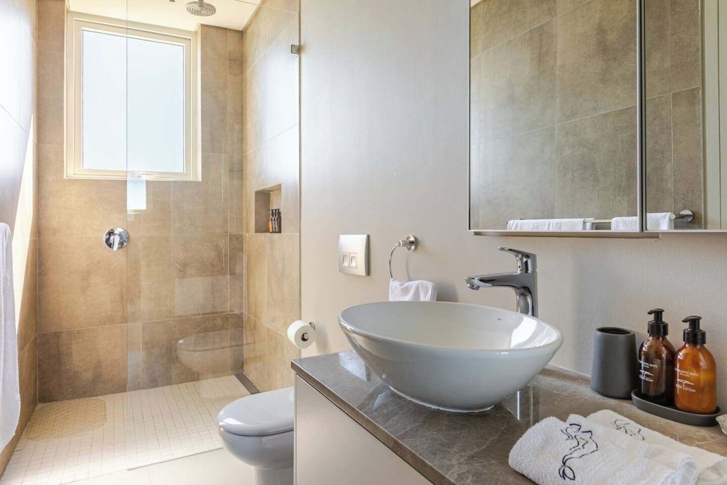 A modern bathroom with a glass-enclosed shower, a white toilet, a large vessel sink, and a mirror above the sink.
