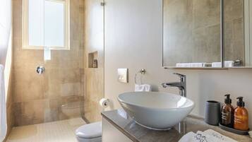A modern bathroom with a glass-enclosed shower, a white toilet, a large vessel sink, and a mirror above the sink.