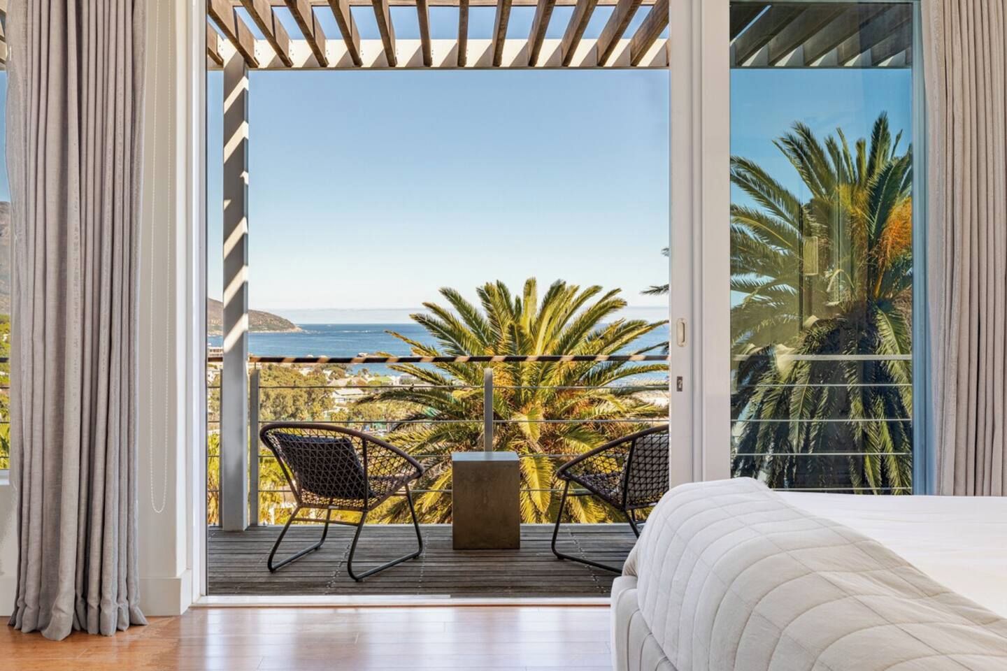 Una camera da letto con un letto, vista sull'oceano e un balcone con sedie.