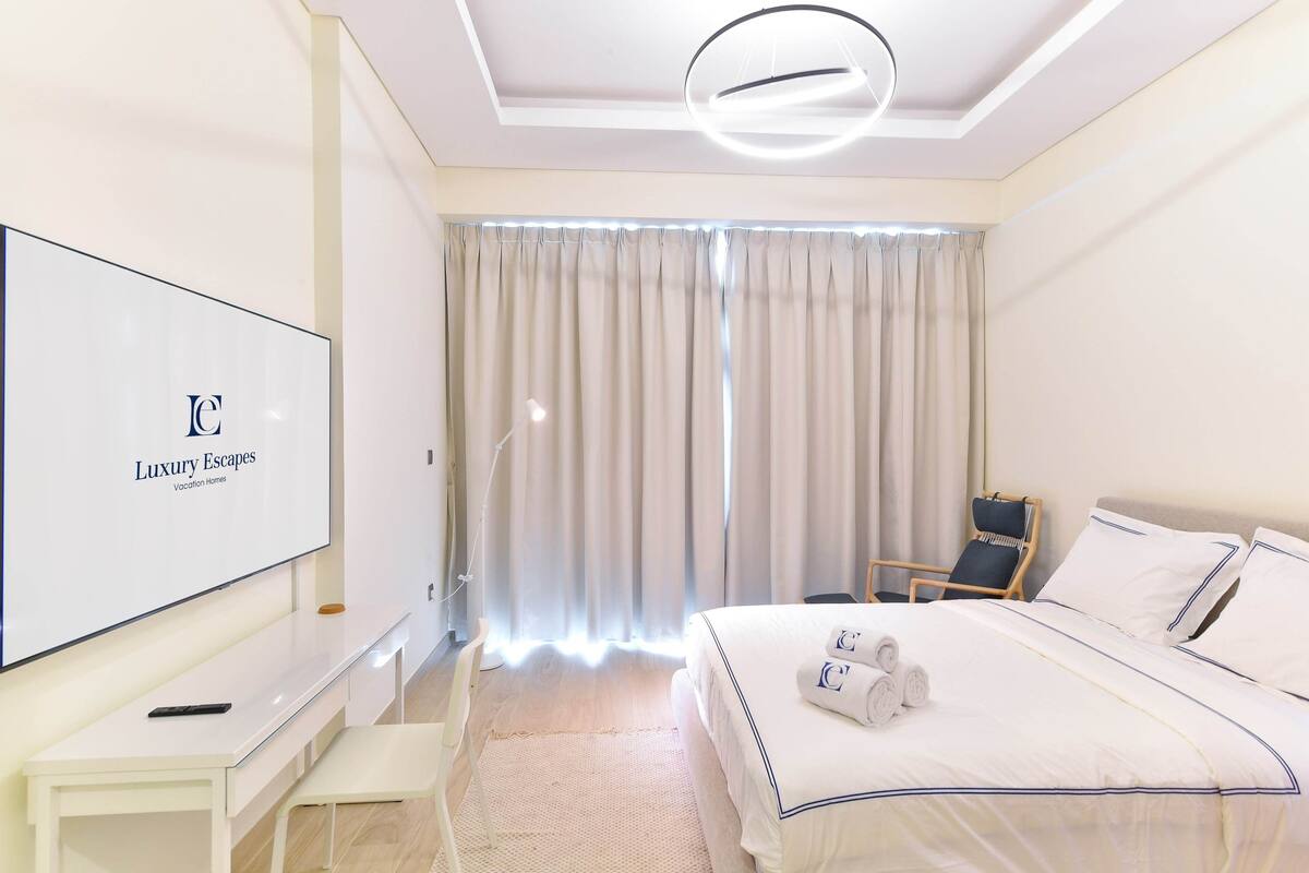 A hotel room with a bed, a desk, a chair, a TV, and curtains.
