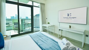 Hotellihuone, jossa on suuri ikkuna, sänky, työpöytä ja televisio, jolta näkyy ohjelma nimeltä ”Luxury Escapes Vacation Homes”.