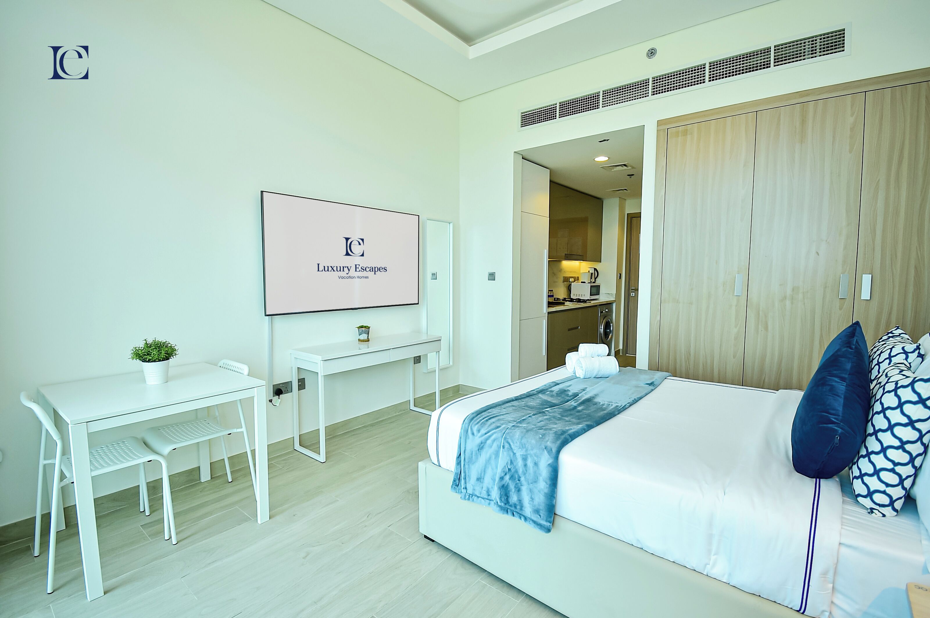 A modern hotel room with a bed, a desk, and a chair. There is a sign on the wall and a wardrobe.
