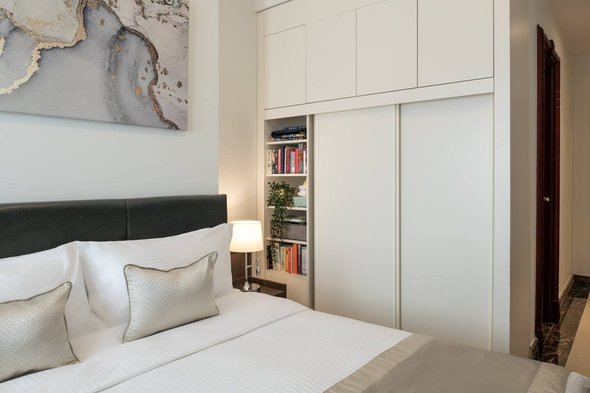 A neatly arranged bedroom with a bed, bedside table, lamp, and a bookshelf.
