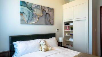 A bedroom with a bed, a teddy bear, a nightstand, a lamp, a wall-mounted artwork, and a built-in wardrobe.