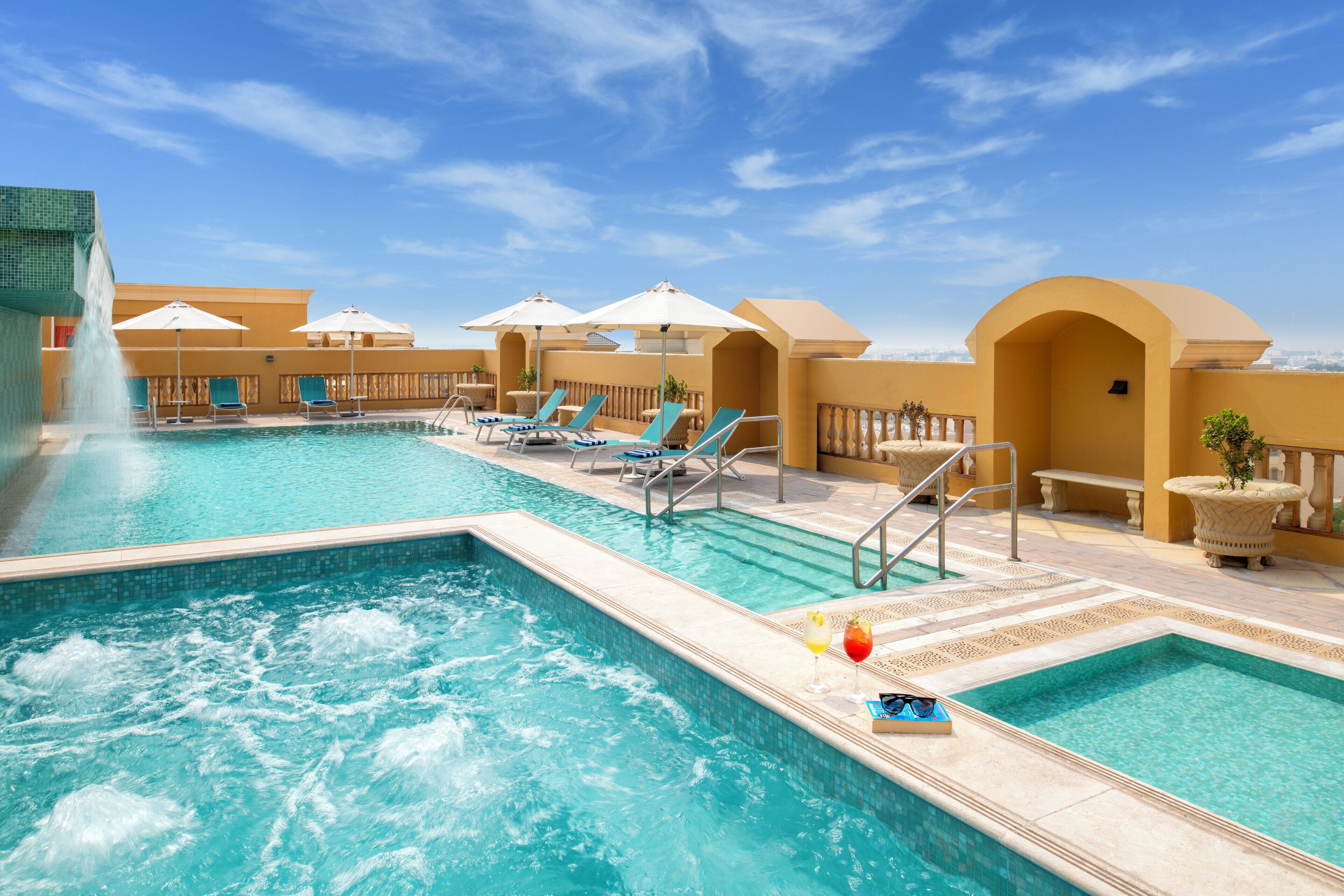 Un área de piscina con sillas de descanso, sombrillas y una fuente de agua.
