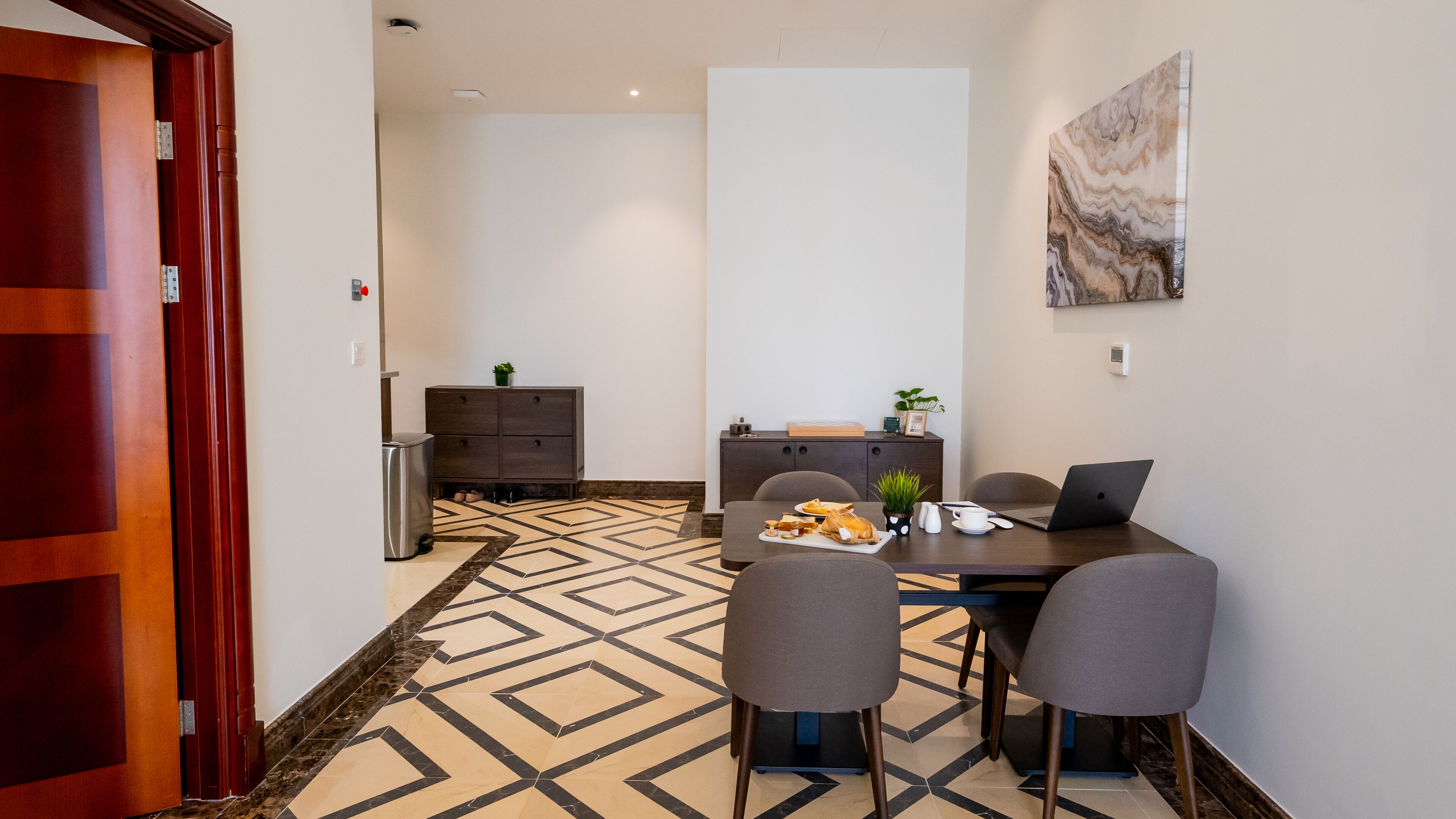 A hotel room with a dining area featuring a table, chairs, and a patterned floor.
