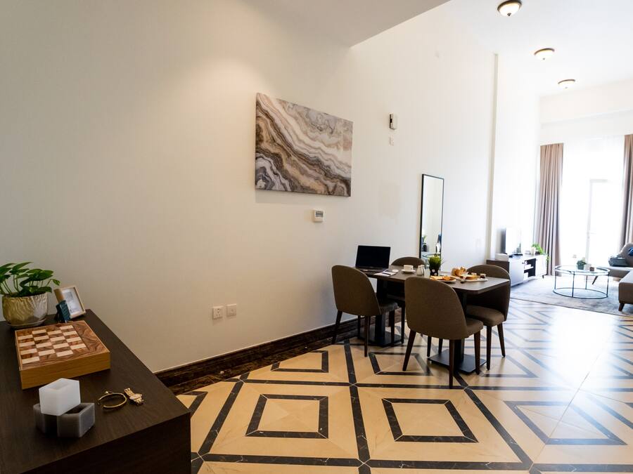 A modern hotel room with a dining area, a large mirror, and a marble artwork on the wall.