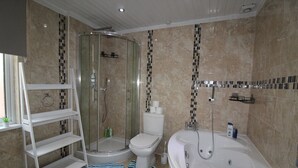 A bathroom with a glass-enclosed shower, a toilet, a bathtub, and a white shelf unit. - St Anns House (Rotherham)