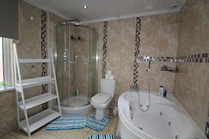 A bathroom with a glass-enclosed shower, a toilet, a bathtub, and a white shelf unit.