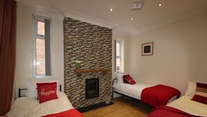 A room with two beds, each with red bedding and pillows, a brick-patterned wall, and a fireplace. - St Anns House (Rotherham)