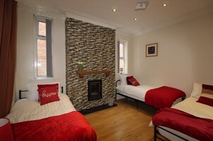 A room with two beds, each with red bedding and pillows, a brick-patterned wall, and a fireplace.