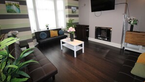 A living room with a sofa, a coffee table, a fireplace, and a TV mounted on the wall. - St Anns House (Rotherham)