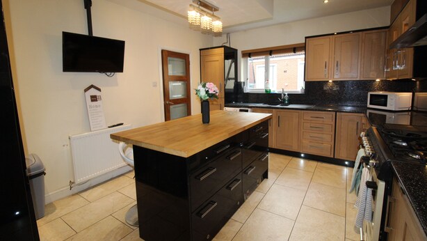 A modern kitchen with a central island, wooden cabinets, a built-in microwave, and a TV mounted on the wall. - St Anns House (Rotherham)