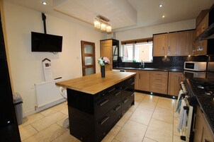 A modern kitchen with a central island, wooden cabinets, a built-in microwave, and a TV mounted on the wall.